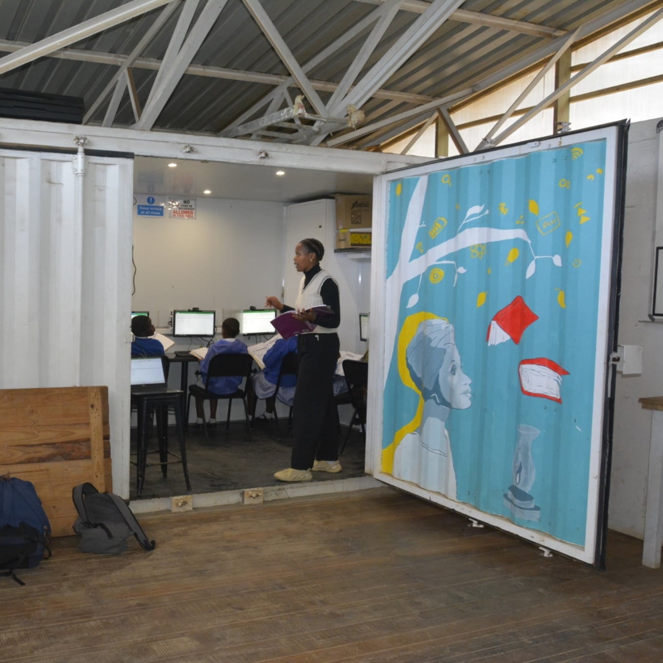 Teacher leading a computer lesson for pupils inside a converted shipping-container classroom